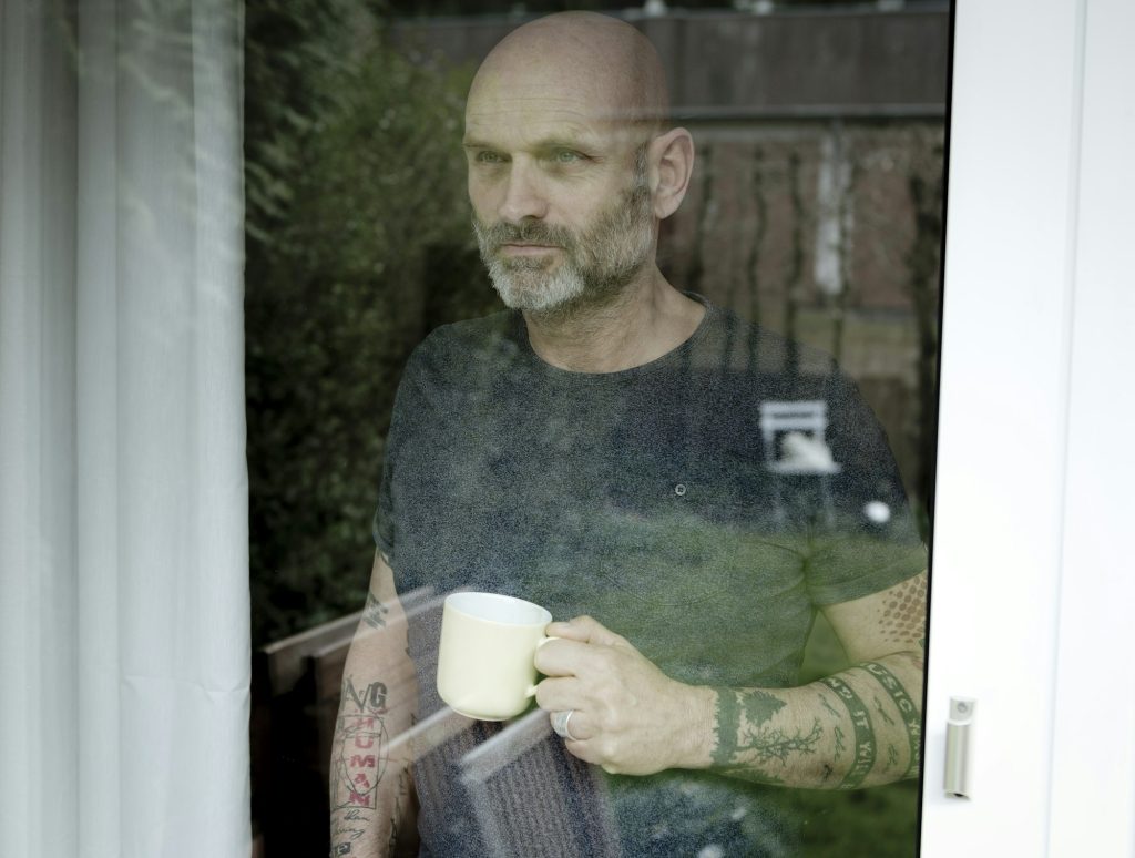 Tattooed man drinking coffee, looking out of window